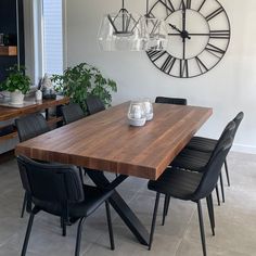 a wooden table with black chairs and a large clock on the wall behind it in a dining room