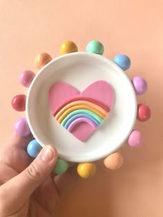 a hand holding a white bowl filled with candy hearts and rainbow candies in it