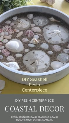 a bowl filled with sand and sea shells on top of a yellow table next to flowers