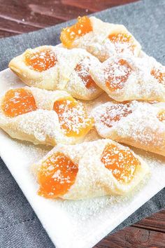 small pastries with powdered sugar and orange toppings on a square white plate