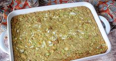 a casserole dish filled with food sitting on top of a wooden table next to a colorful cloth