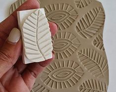 a hand holding a rubber stamp with a leaf design on it's back side