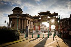 the sun shines brightly in front of an arch on a city street with tall buildings