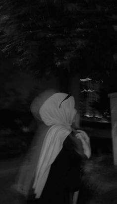 black and white photograph of a woman walking down the street with a scarf on her head