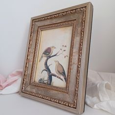 two birds sitting on a tree branch in a framed picture next to some tissue paper