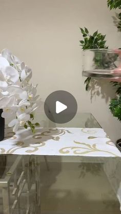 a glass table topped with white flowers next to a potted plant