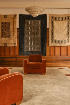 a living room with two orange chairs and rugs on the wall