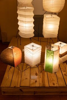 four paper lanterns are sitting on a wooden table with two lamps in the shape of rectangles