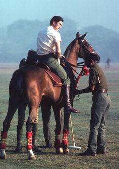 two men standing next to each other on top of a brown horse in a field