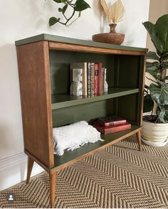 a green bookcase with books and plants on top