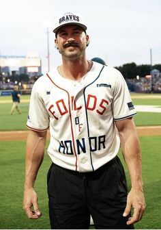 a man with a mustache standing in the outfield at a baseball game wearing a uniform