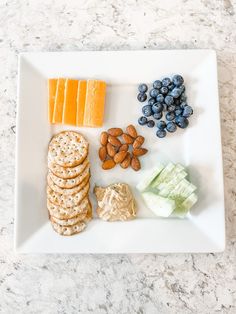 a white plate topped with crackers and cheese next to blueberries, nuts and grapes