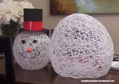 two snowmen made out of yarn sitting on a desk next to a vase with flowers