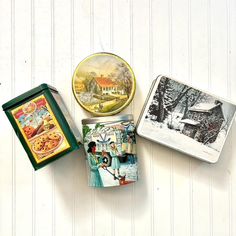 three small tins with pictures on them sitting next to each other in front of a white wall