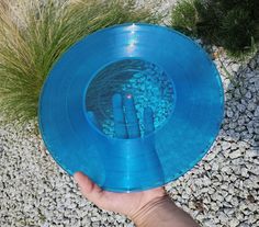 a hand holding a blue frisbee on top of a gravel ground next to grass