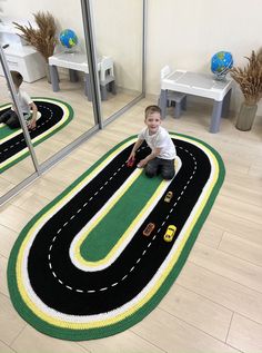 a little boy sitting on the floor in front of a rug that looks like a road