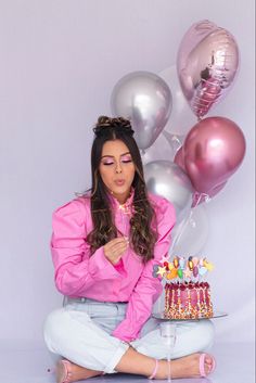 a woman sitting in front of a cake and balloons