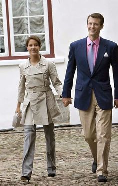 a man and woman walking down a cobblestone street holding hands, both dressed in business attire