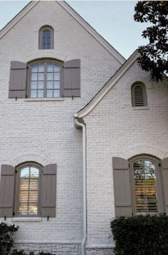 a large white brick house with shutters open