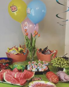 a table topped with watermelon, melons and other foods on plates next to balloons