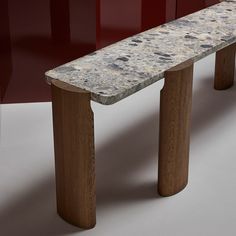 a marble bench sitting on top of a white floor next to red walls and wooden legs