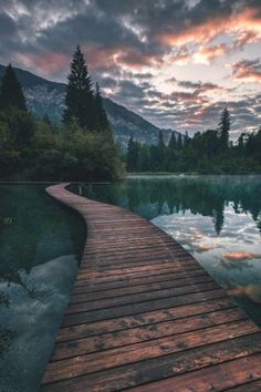 a wooden walkway leading to a body of water with mountains in the background at sunset