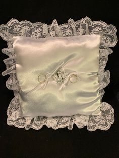 a white pillow with two wedding rings on it and lace trimming around the edges