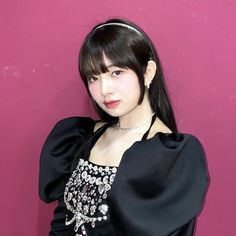 a young woman posing in front of a pink wall wearing a black top and silver necklace