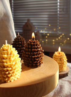 three pine cone candles sitting on top of a wooden table next to a white pillow