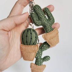 a hand holding a green cactus keychain in it's left hand,