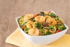 a white bowl filled with shrimp and veggies on top of a yellow napkin