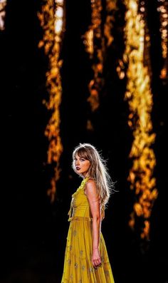 a woman in a yellow dress is walking through the woods with her hand on her hip