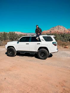 a man sitting on top of a white suv in the desert