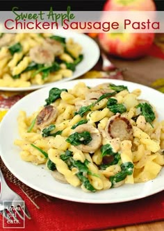 two white plates filled with pasta and spinach on a table cloth next to an apple