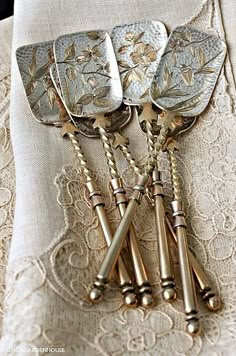 four antique silverplated serving utensils sitting on top of a lace tablecloth