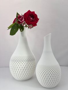 two white vases with red roses in them on a table top next to each other