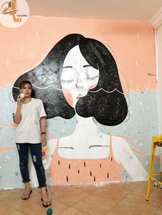 a woman standing in front of a wall with a painting on it's side