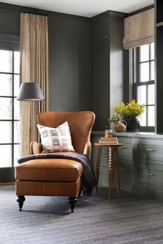 a brown chair sitting in front of a window next to a table with a lamp on it