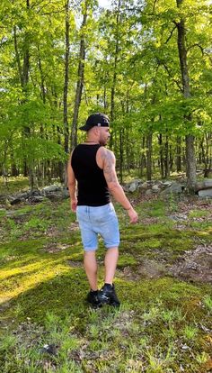 a man in black shirt and blue shorts standing on grass with trees in the background