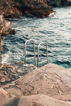 an empty swimming pool on the edge of a cliff next to the ocean and rocky shore