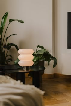 there is a table with a lamp on it in the room next to some plants