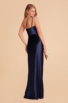 a woman in a long blue dress with her back turned to the camera, wearing a gold clutch