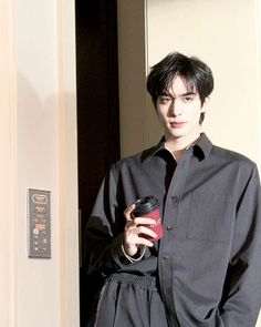 a man standing in front of a door holding a cup and looking at the camera