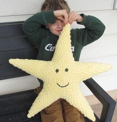 a young boy sitting on a bench holding up a crocheted starfish pillow