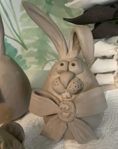 two ceramic rabbits sitting next to each other on top of a white cloth covered table