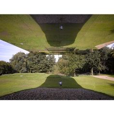 the shadow of a person standing under an overhang in a park with trees and grass