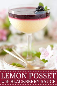 a glass filled with liquid and topped with blackberries on top of a plate next to flowers