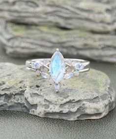 a white gold ring with an opal and rainbow stones in the center on top of a rock