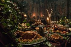 a table full of food with candles and deer heads on the wall in the background