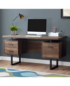 a computer desk with two drawers and a monitor on it, in front of a gray wall